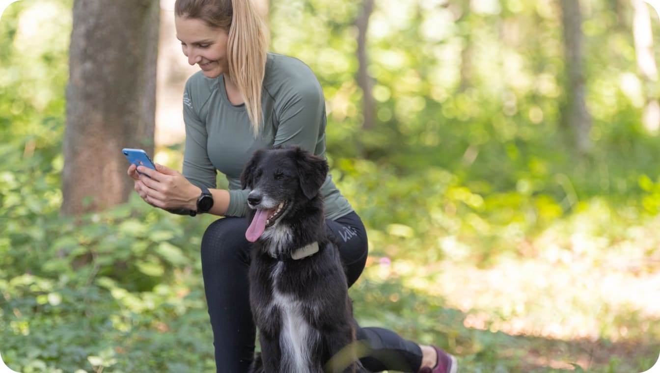 Koira, jolla on Tractive GPS -koirapaikannin, istuu lenkille valmistautuvan omistajan vieressä