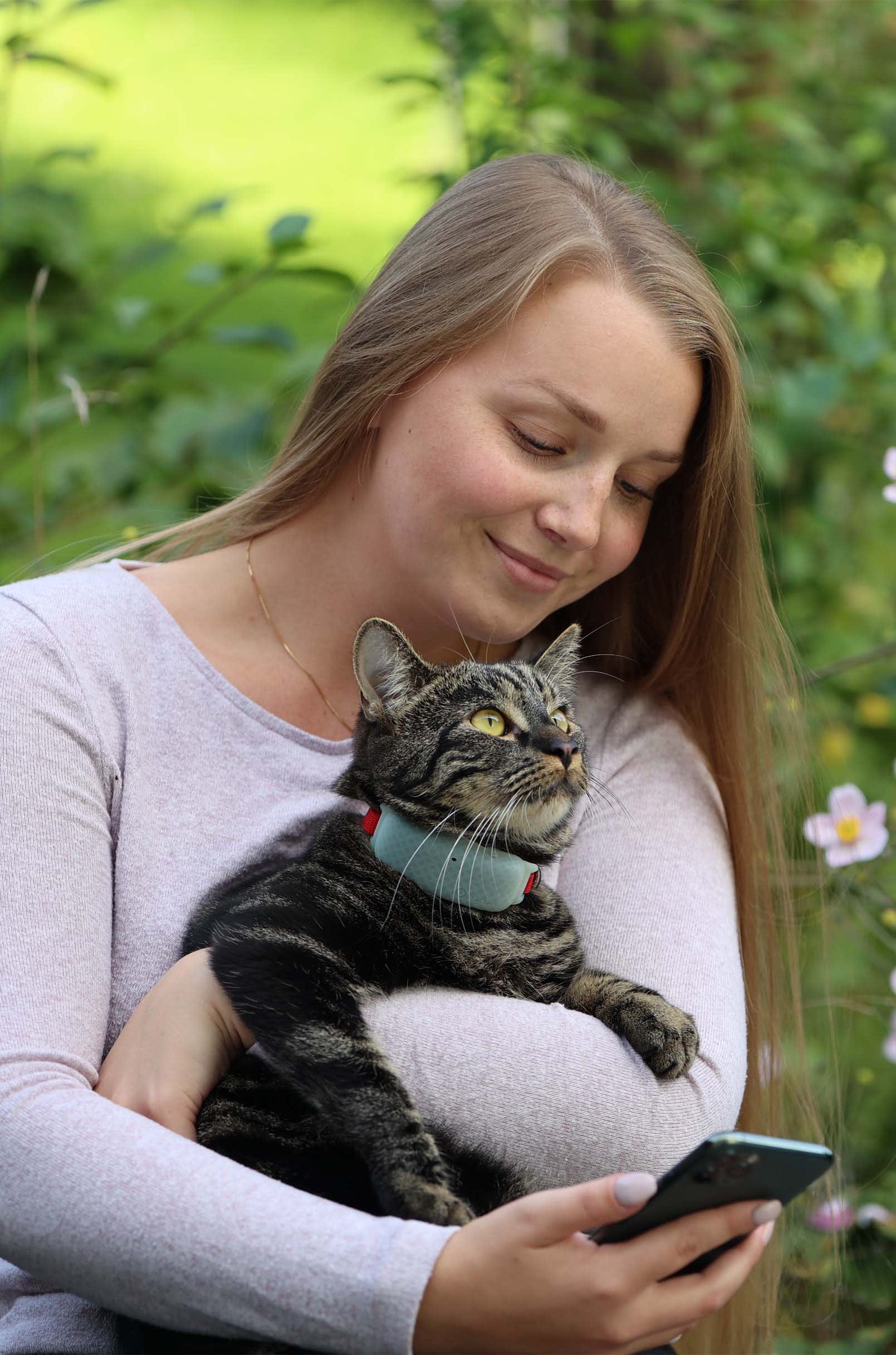Katze mit Tractive GPS Tracker für Katzen und Besitzer:in sitzen im Freien