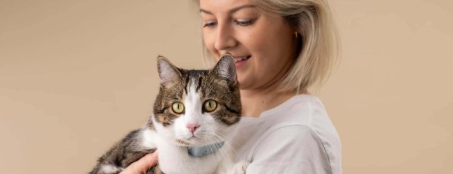 Une jeune femme blonde tenant un chat tigré dans ses bras, qui porte un traceur afin de mesurer sa fréquence cardiaque