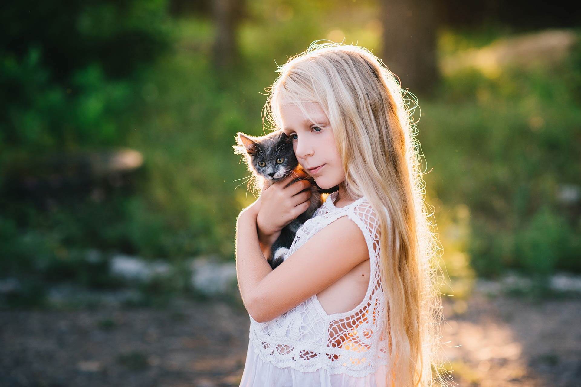 niña rubia con el pelo largo en el patio abrazando a un gato