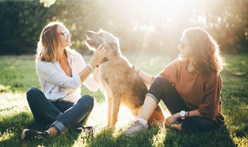 two woman sitting down outdoors with a dog
