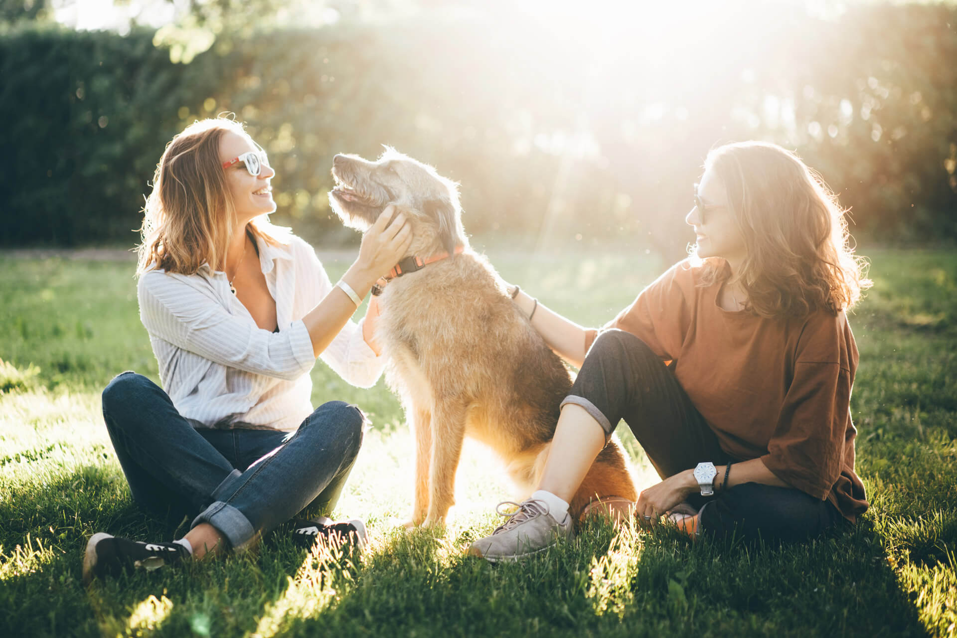 two woman sitting down outdoors with a dog