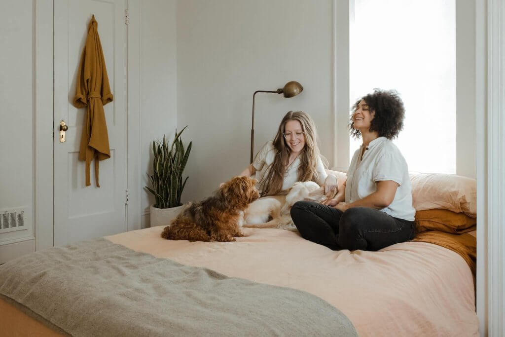 two women and two dogs sitting on a bed 