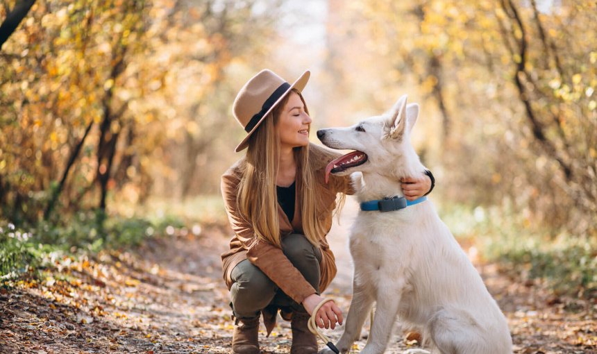 Donna in un bosco con un cane bianco che indossa un localizzatore Tractive GPS per cani