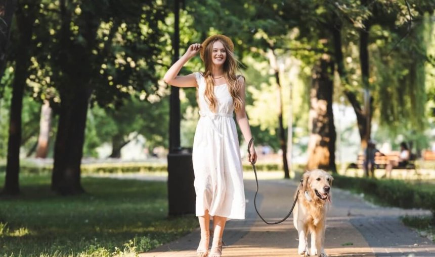 giovane donna con un vestito bianco porta il suo cane al guinzaglio
