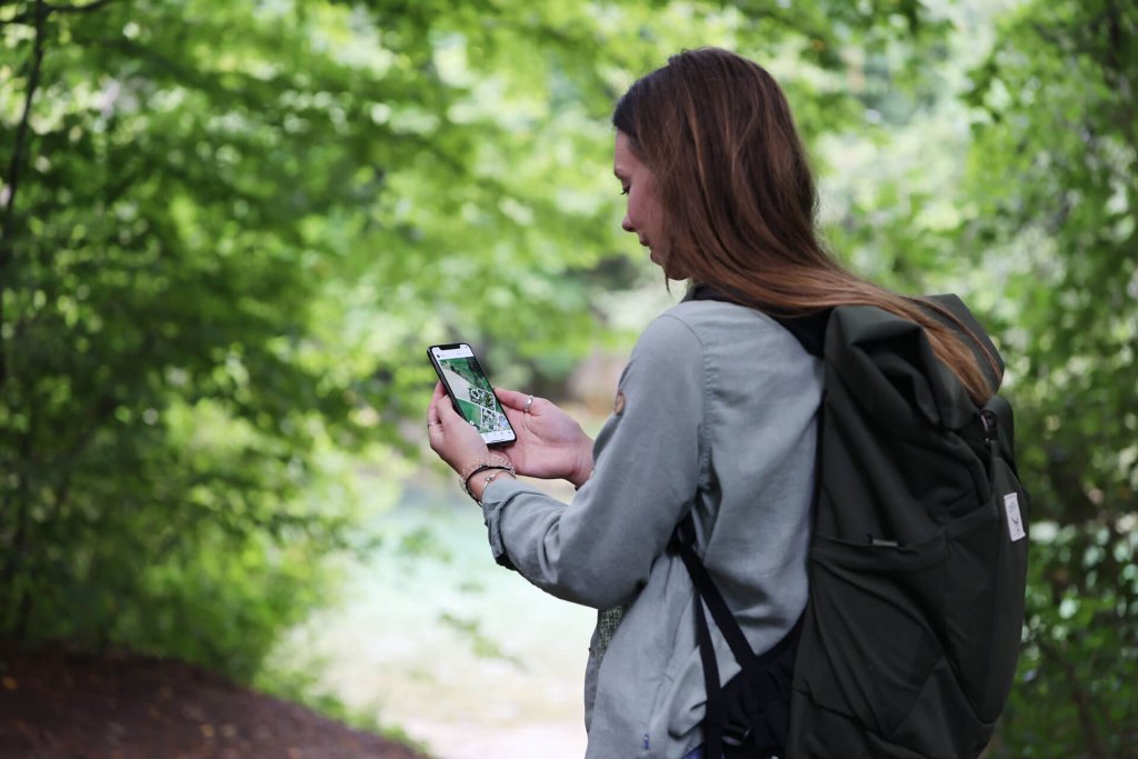 woman in the forest looking at the tractive gps app on a smartphone