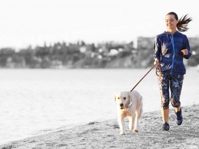 femme faisant du jogging sur la plage avec son chien à la laisse qui porte un GPS Tractive