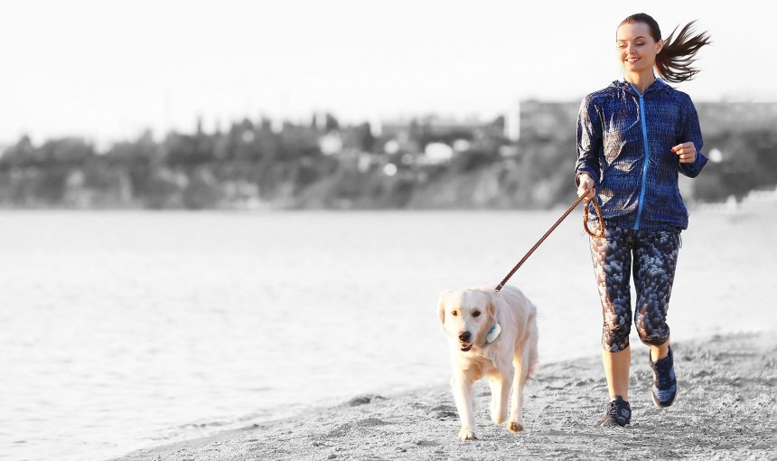 Entlang eines Ufers joggende Frau mit Hund