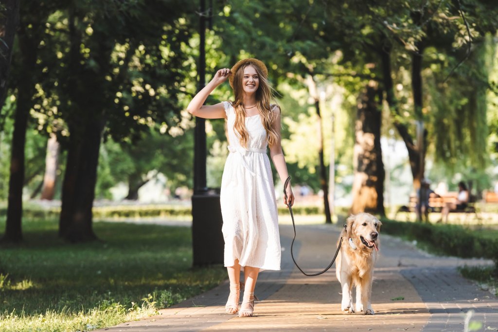 woman in white dress walking golden retriever dog on a leash outdoors, dog wearing Tractive GPS tracker