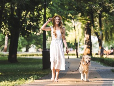 woman in white dress walking dog on a leash down the sidewalk