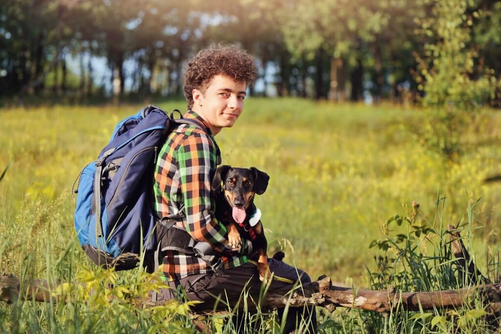 Jeune homme assis sur une branche portant un sac a dos et son chien portant un GPS tractive