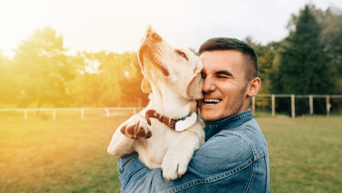 En glad mann som gir hunden sin en klem. Hunden har på seg et Tractive GPS-halsbånd