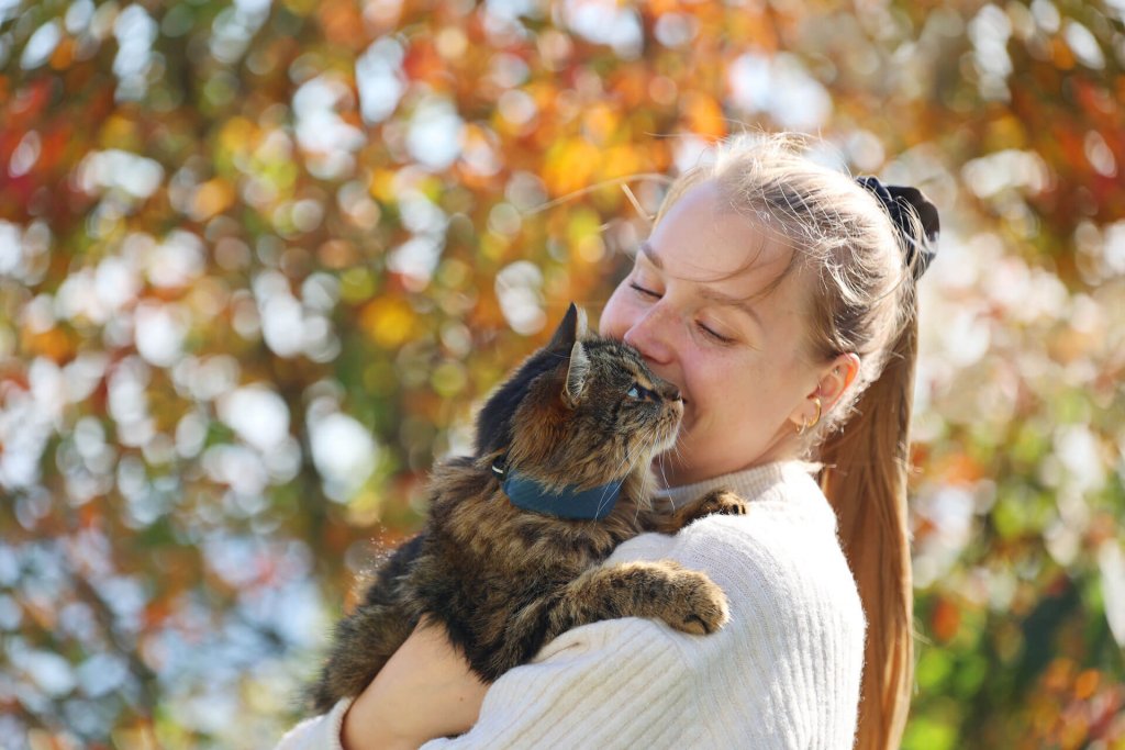 woman holding a brown cat wearing a Tractive GPS cat tracker outside
