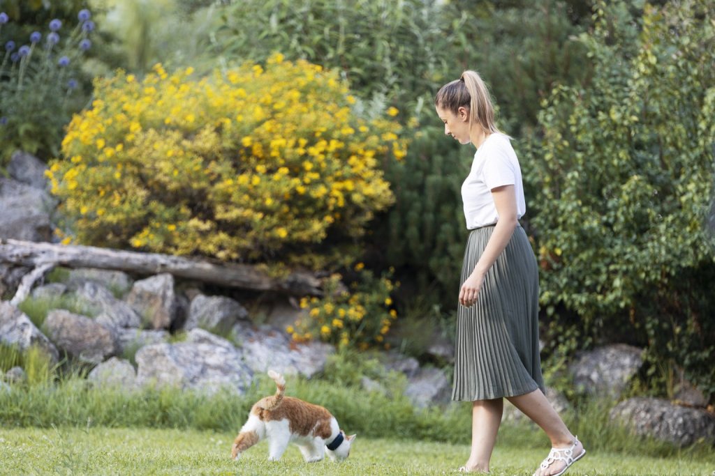 Frau geht mit ihrer Katze, die einen Tractive GPS Tracker am Halsband trägt, im Garten spazieren