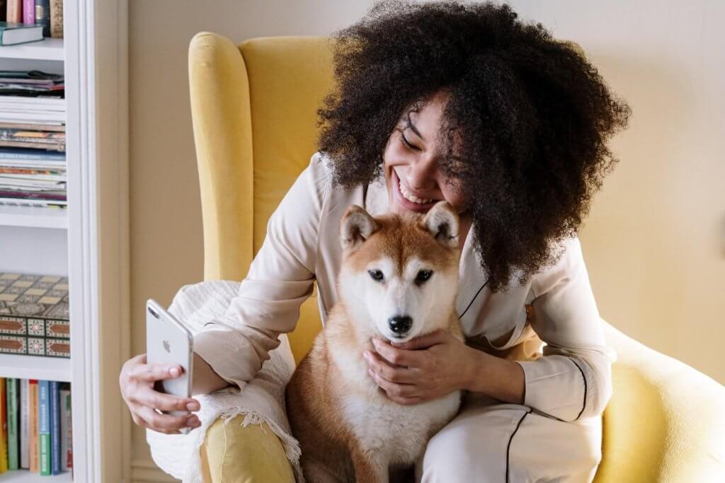 donna siede su una poltrona gialla con un cane, tenendo in mano un'Iphone