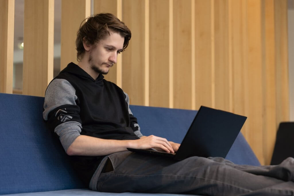 man sitting on a blue couch working on laptop