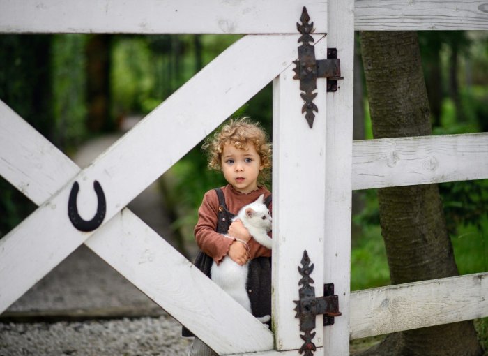 A child holding a cat standing by a fence