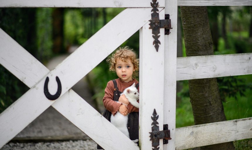 A child holding a cat standing by a fence