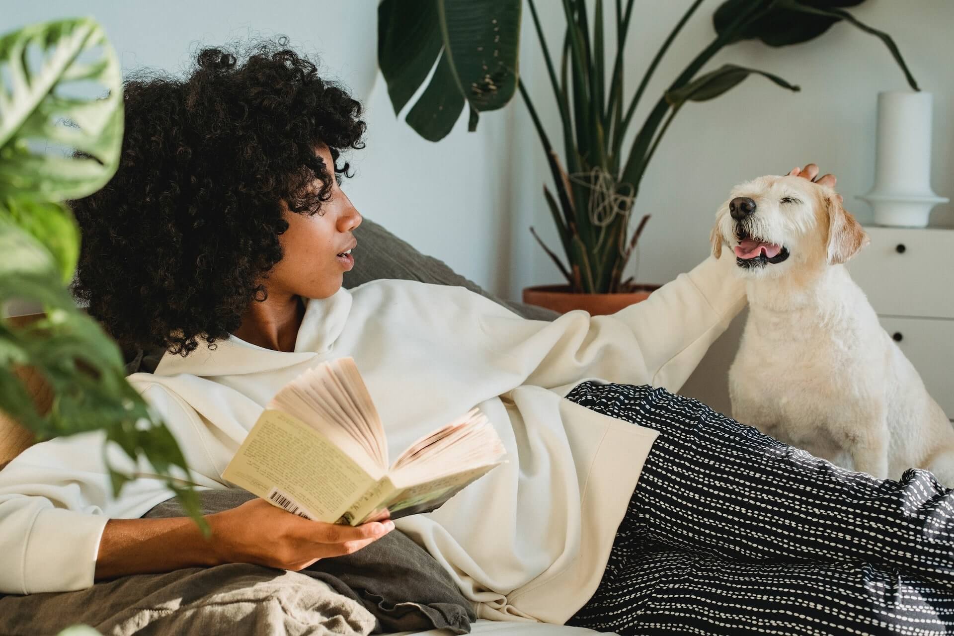 woman lounging in a chair with a book petting dog 