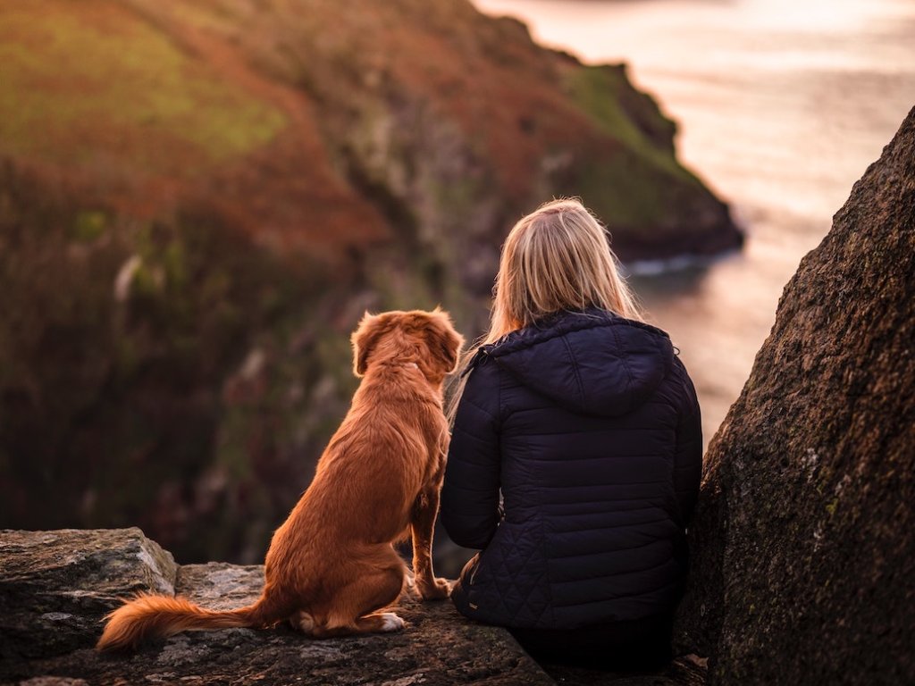 Frau und Hund sitzen auf einem Felsen und schauen in die Ferne