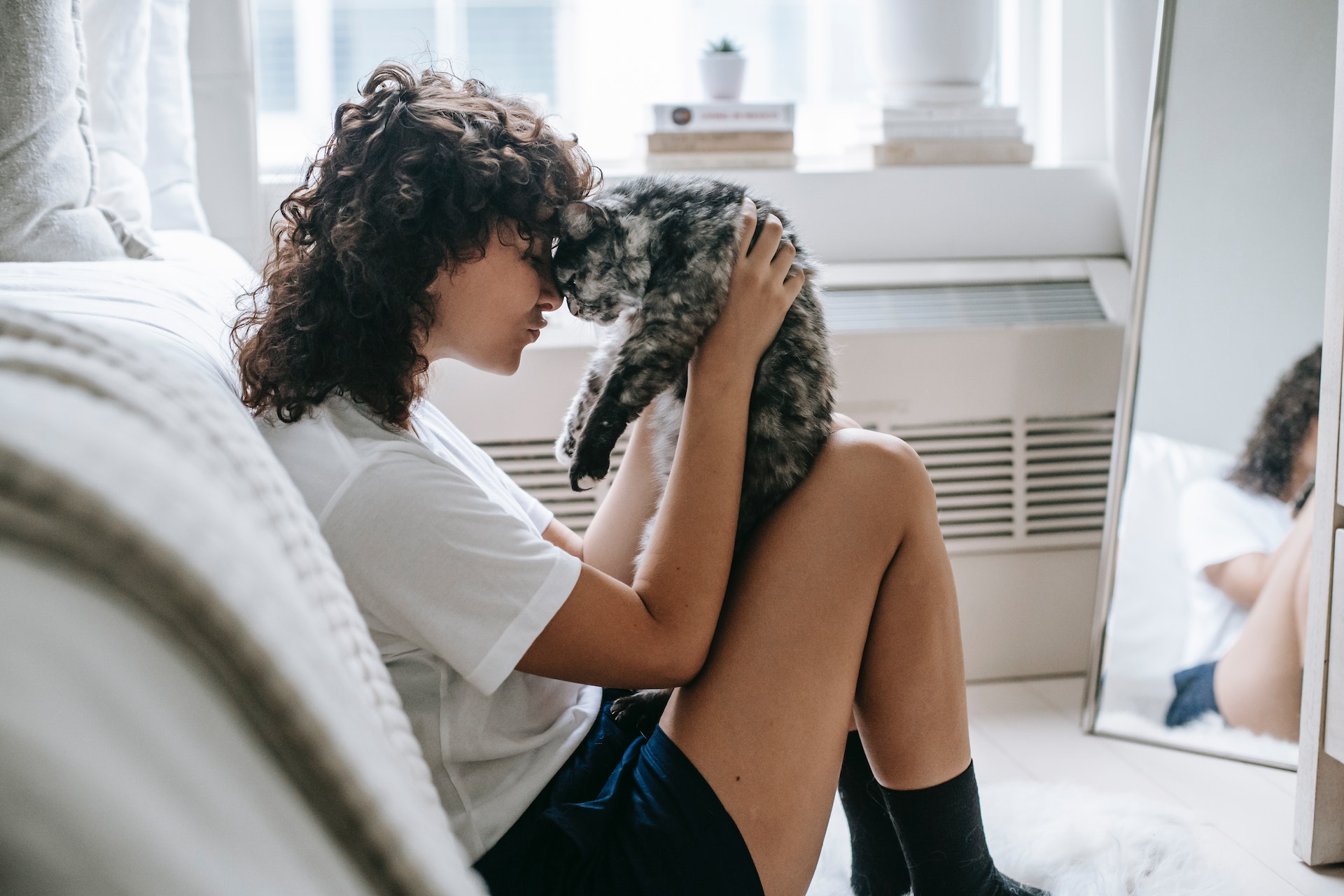 A woman cuddling with her cat near a bed