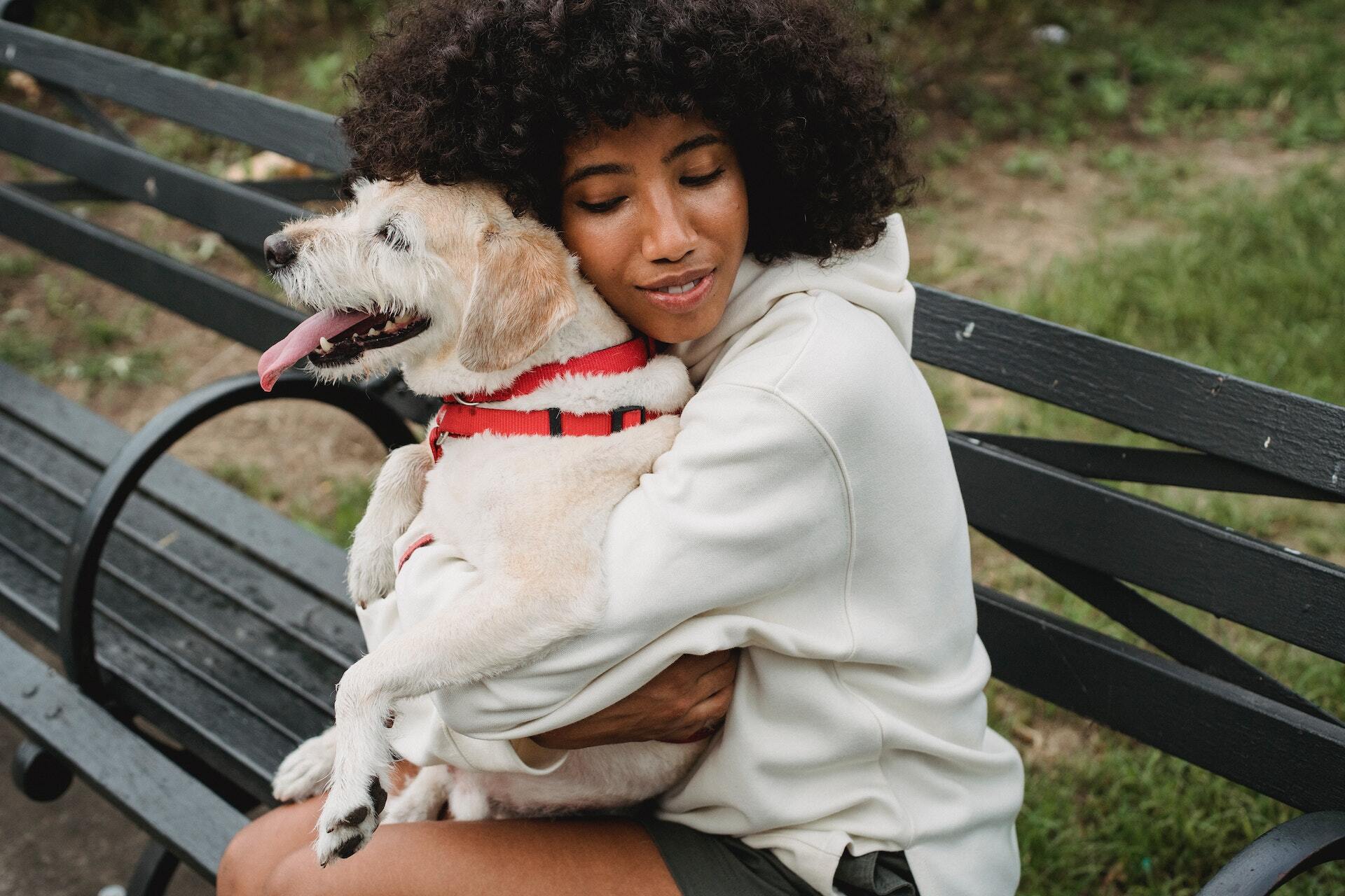 Een vrouw die haar hond knuffelt die een rood tuigje draagt