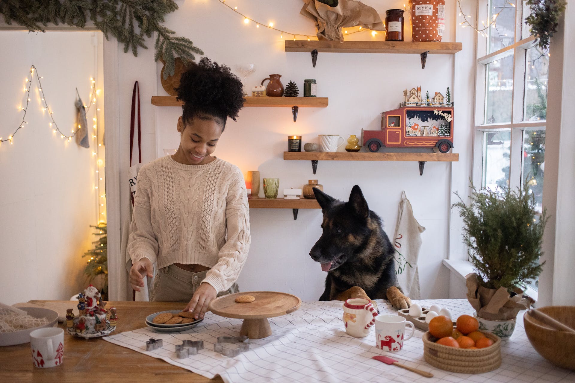 A girl placing cookies on a plate in a kitchen with her dog next to her