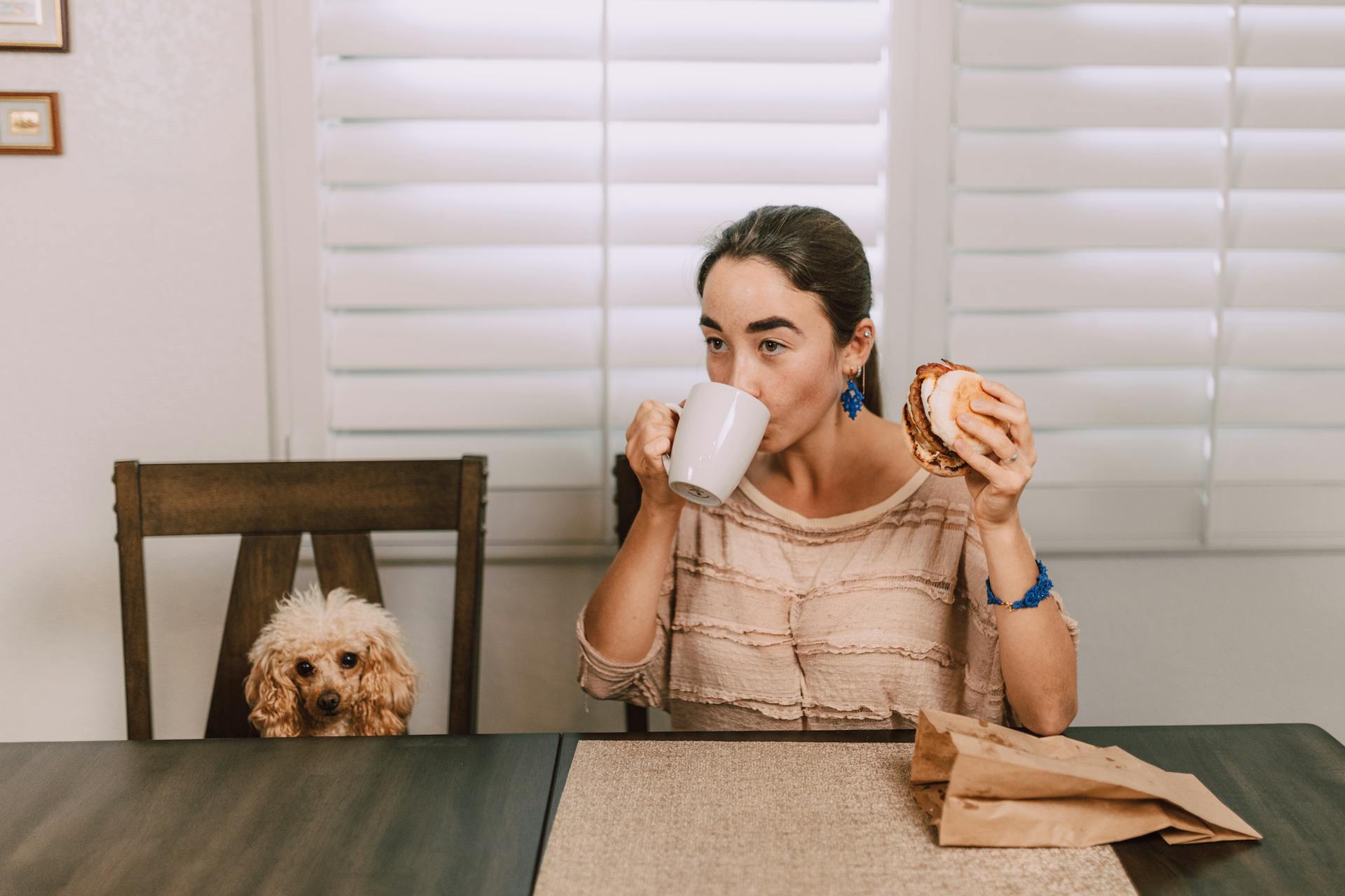 A woman eating a burger next to a puppy on a table