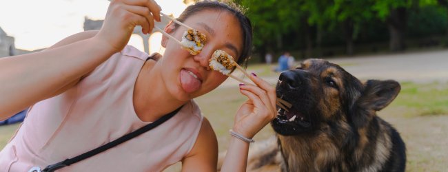A woman posing with sushi on chopsticks next to her dog