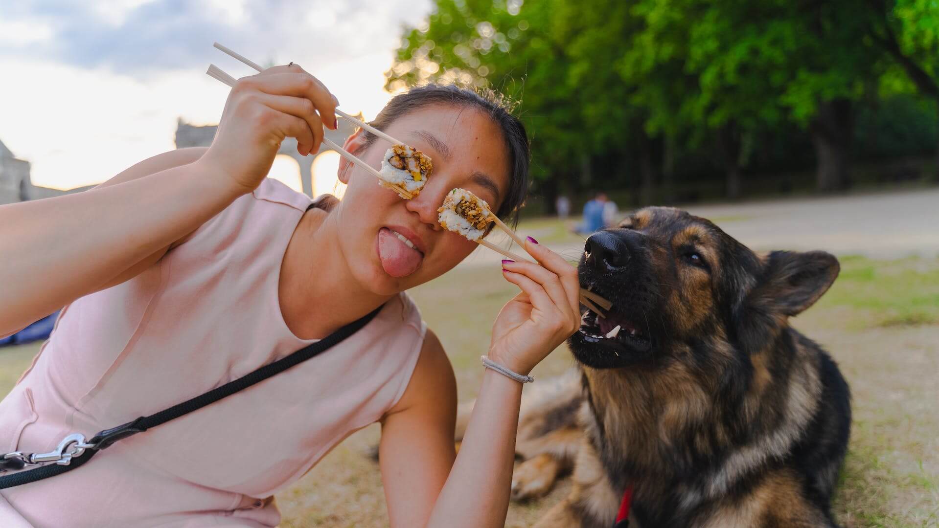 A woman posing with sushi on chopsticks next to her dog