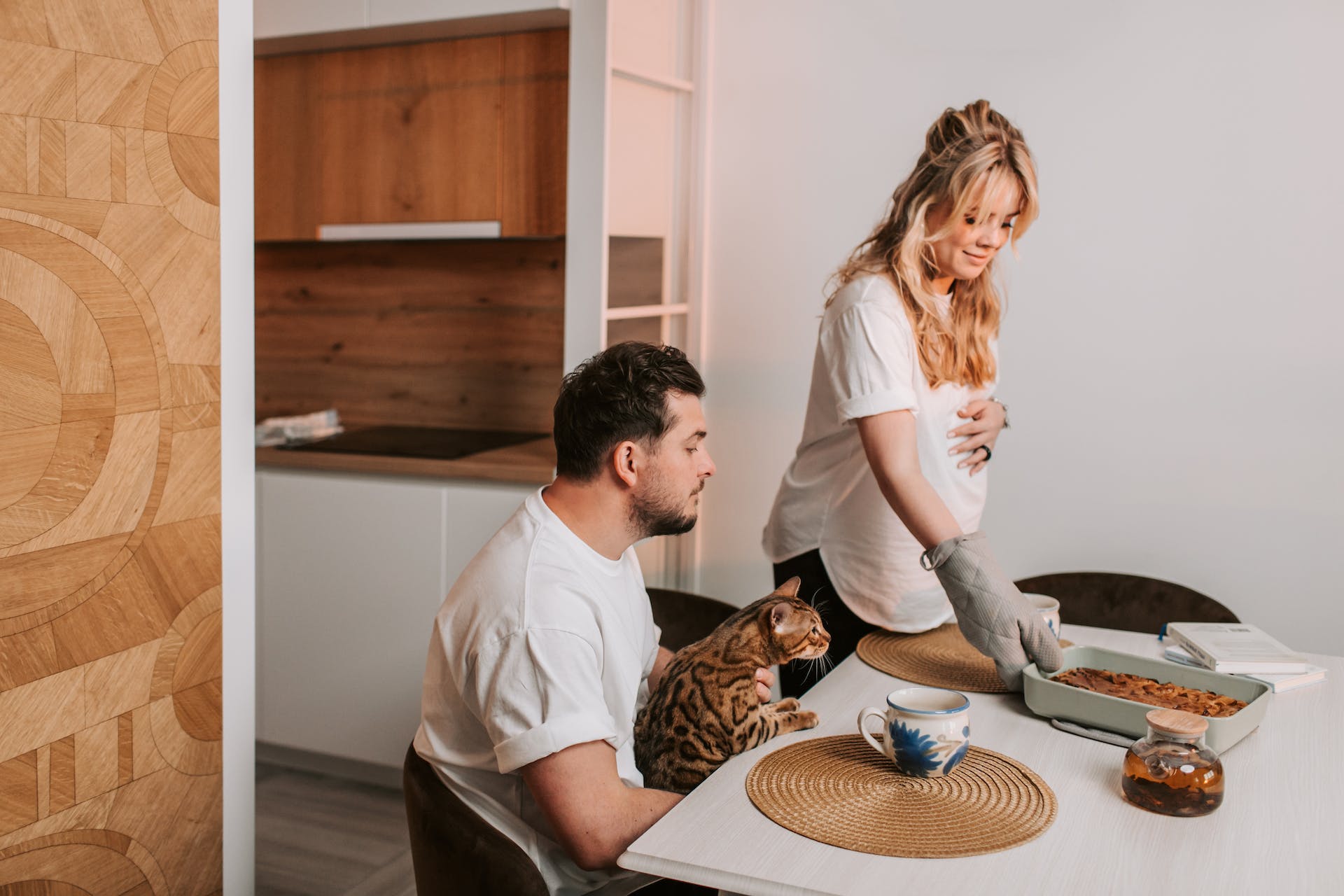 A couple sitting at a table with their cat and a baked cake