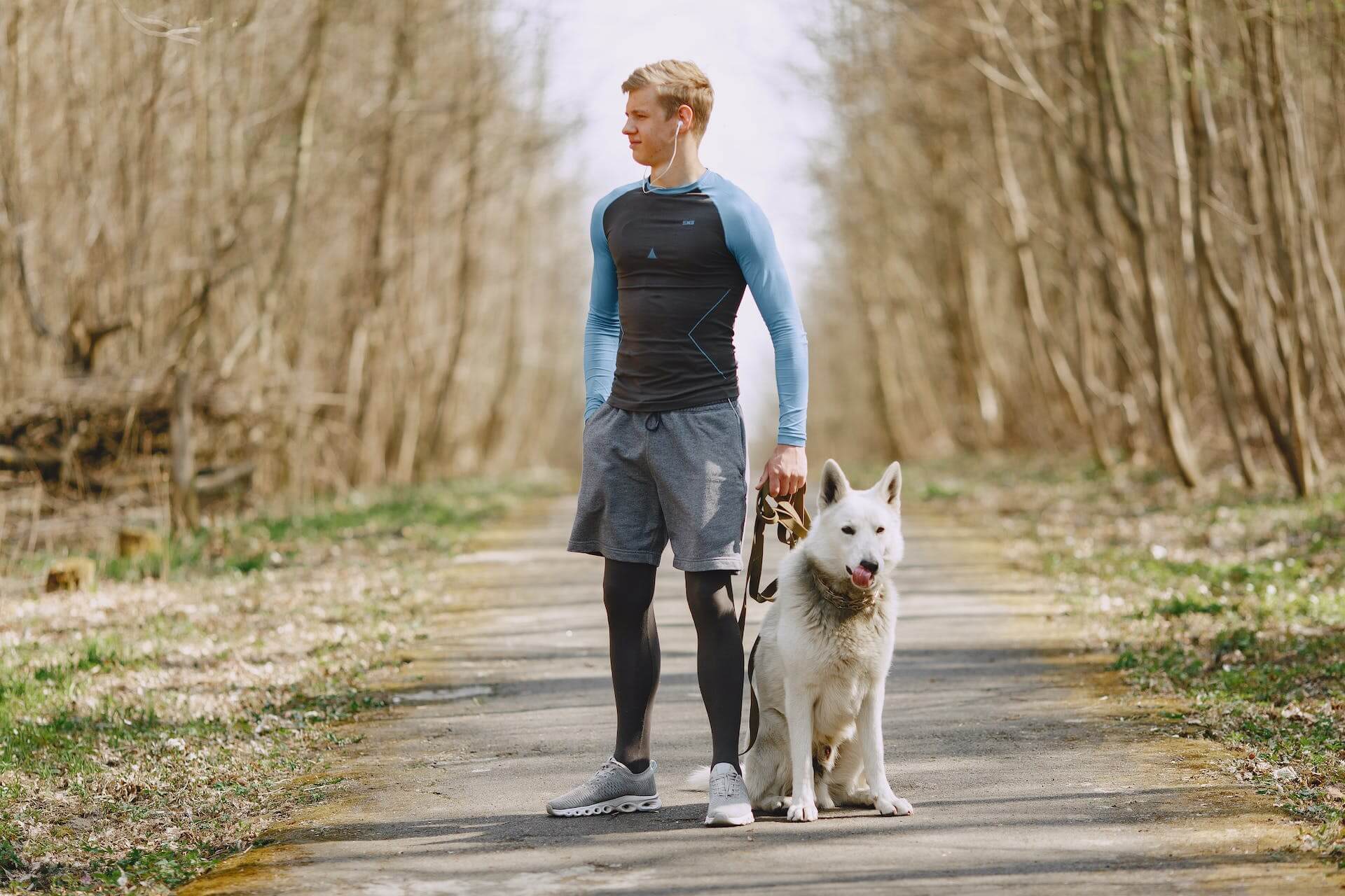A runner standing by a dog in a forest trail