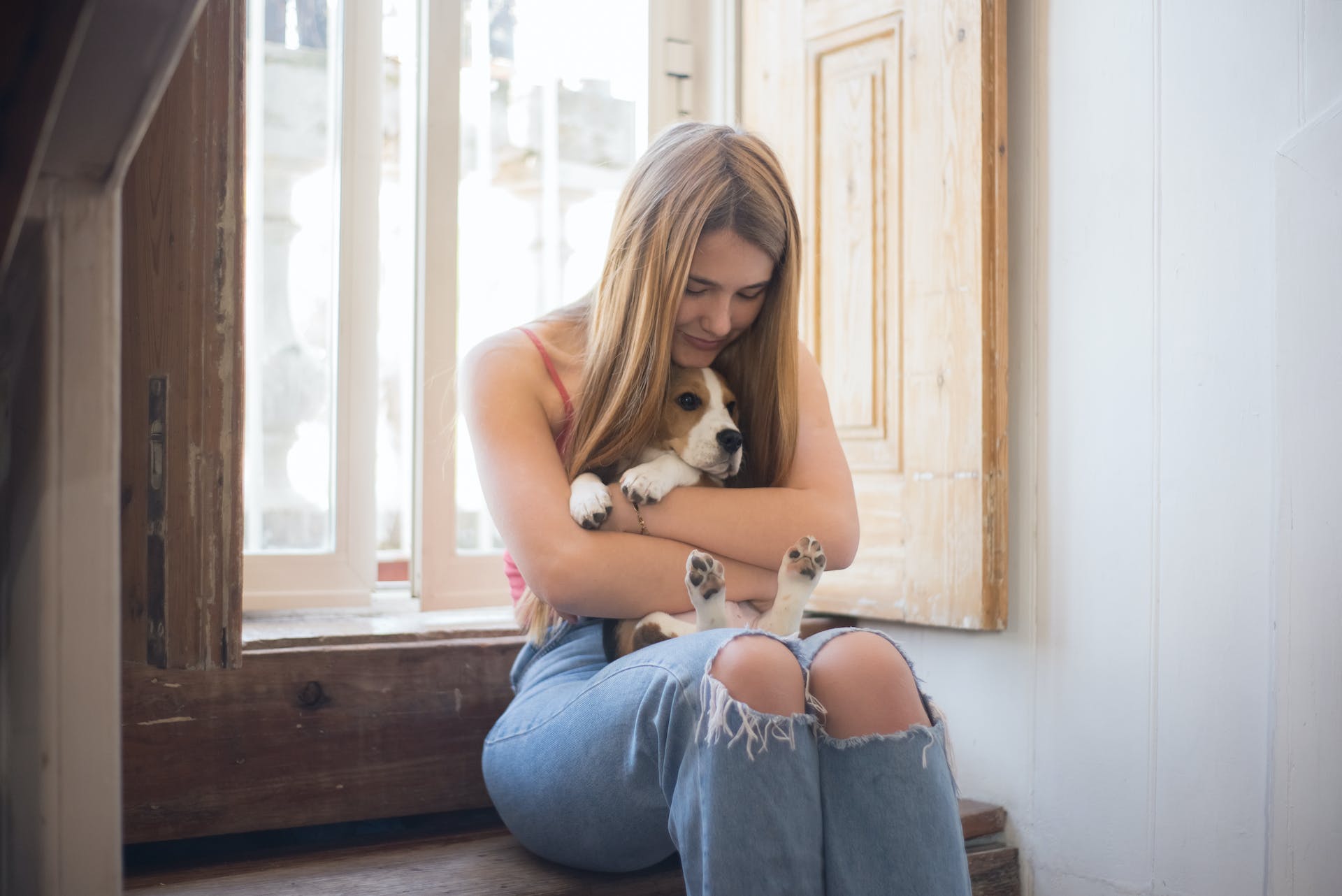 jeune femme assise sur le rebord d'une fenêtre tenant un beagle dans ses bras