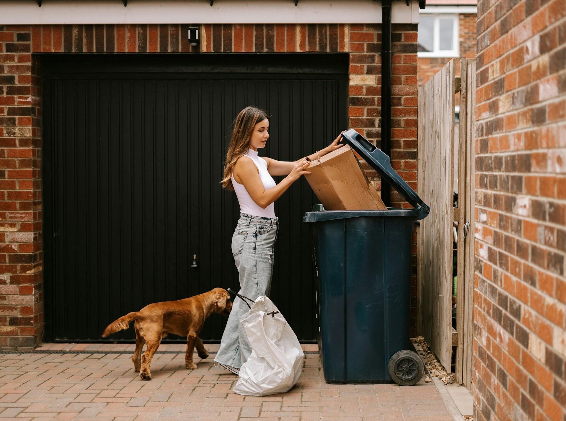 A woman throwing away her trash accompanied by her dog