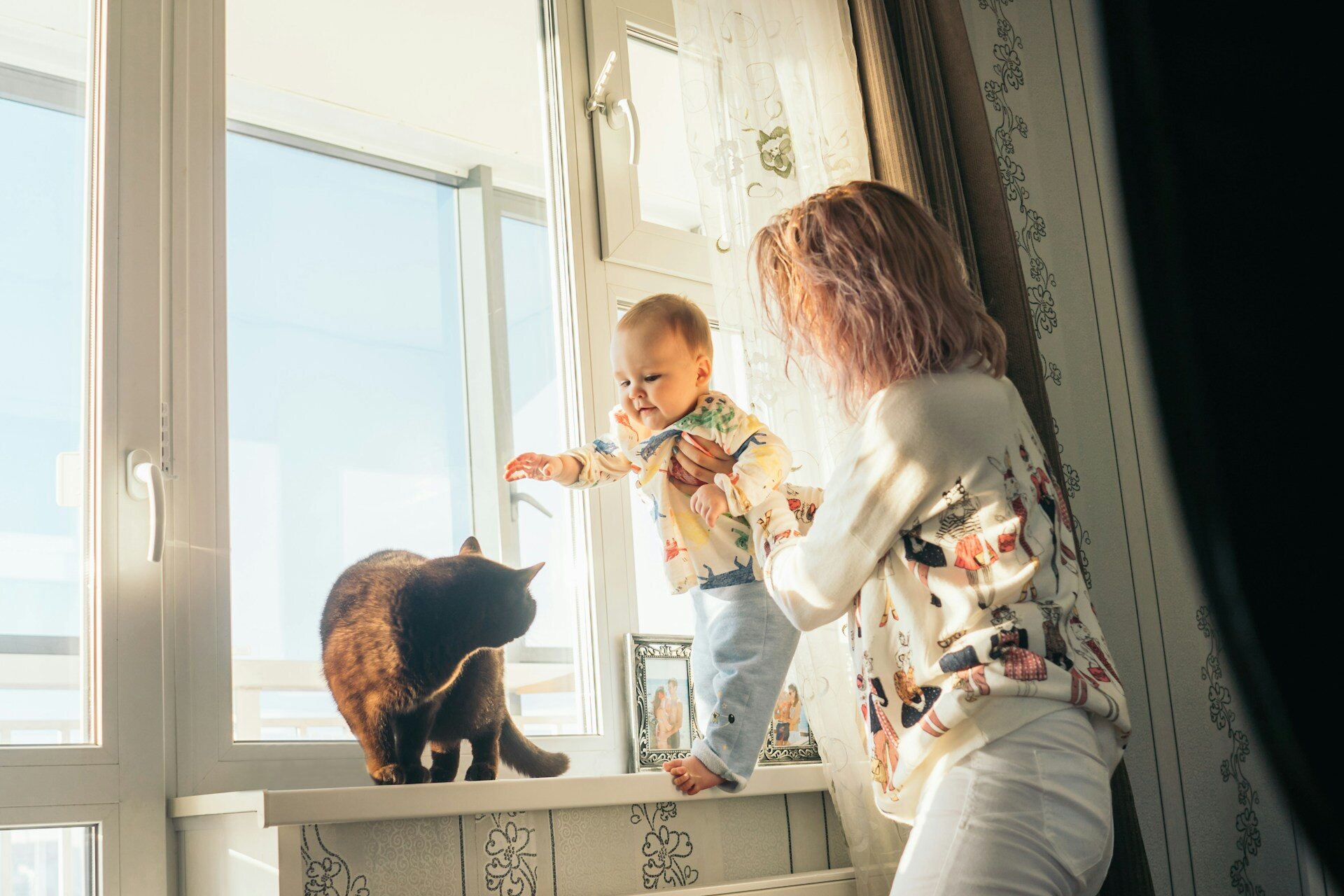 A woman and baby playing with a cat by the window