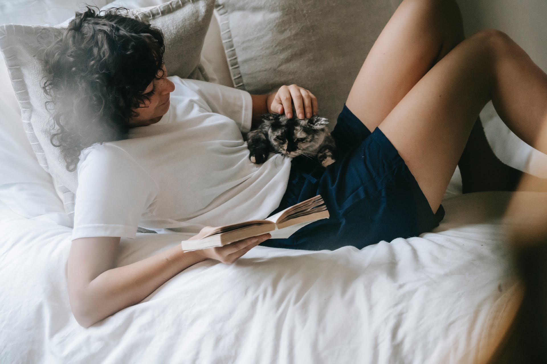 A woman cuddling with a cat in bed while reading a book