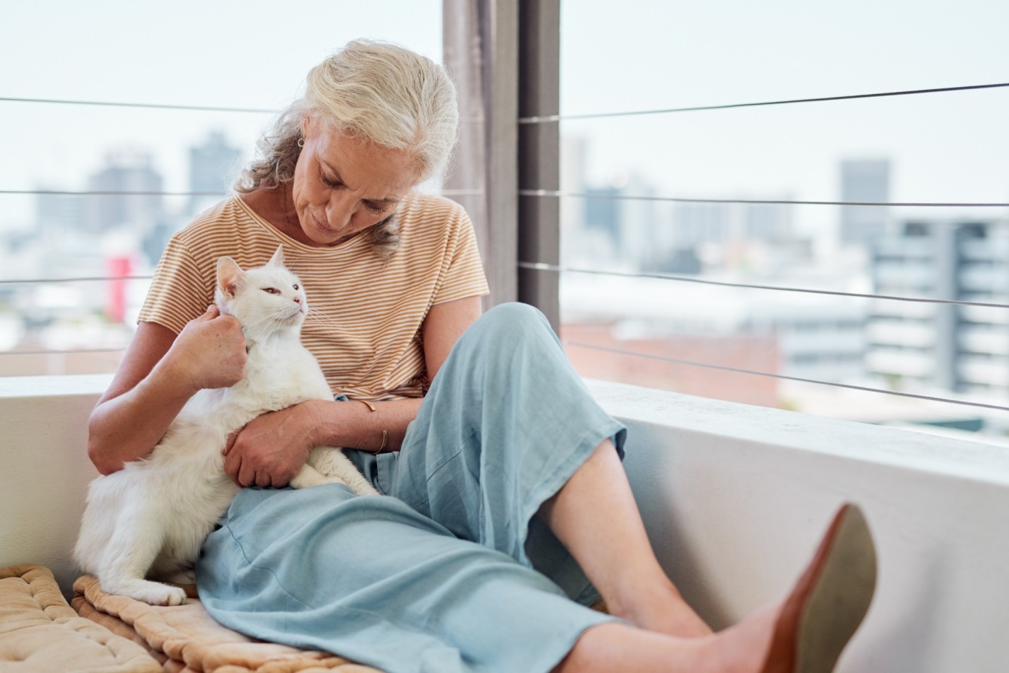 A woman sitting by a cat proof balcony with her cat