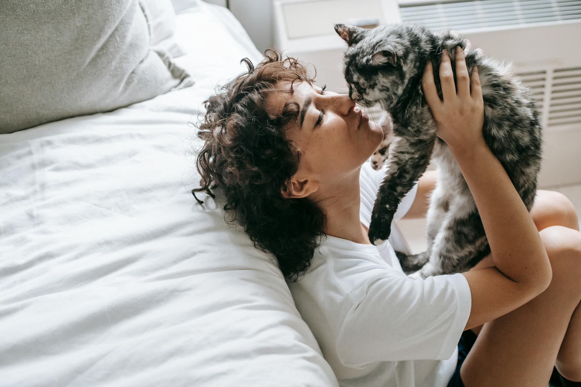 A woman cuddling her cat next to a bed