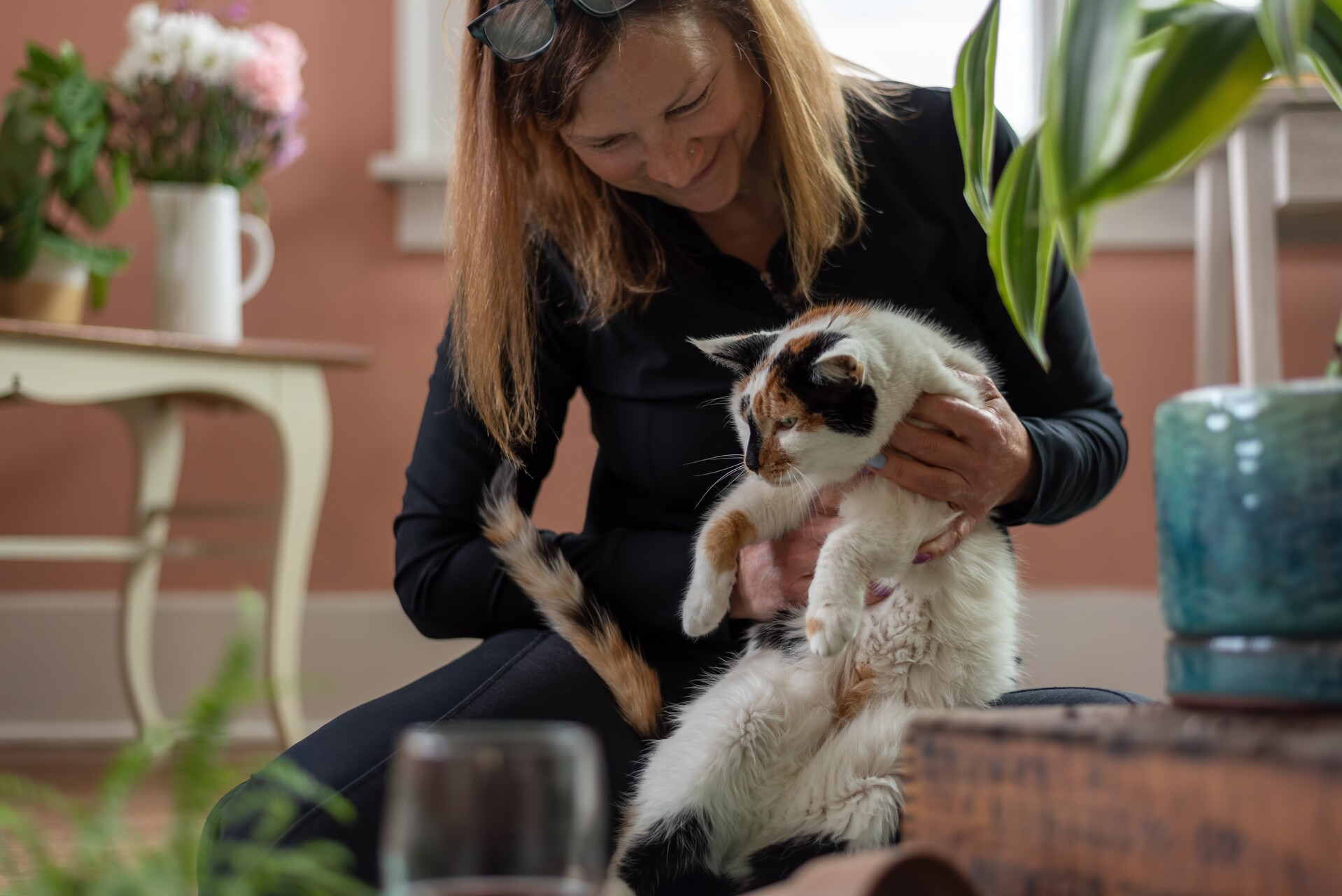A woman sitting with a cat next to indoor plants