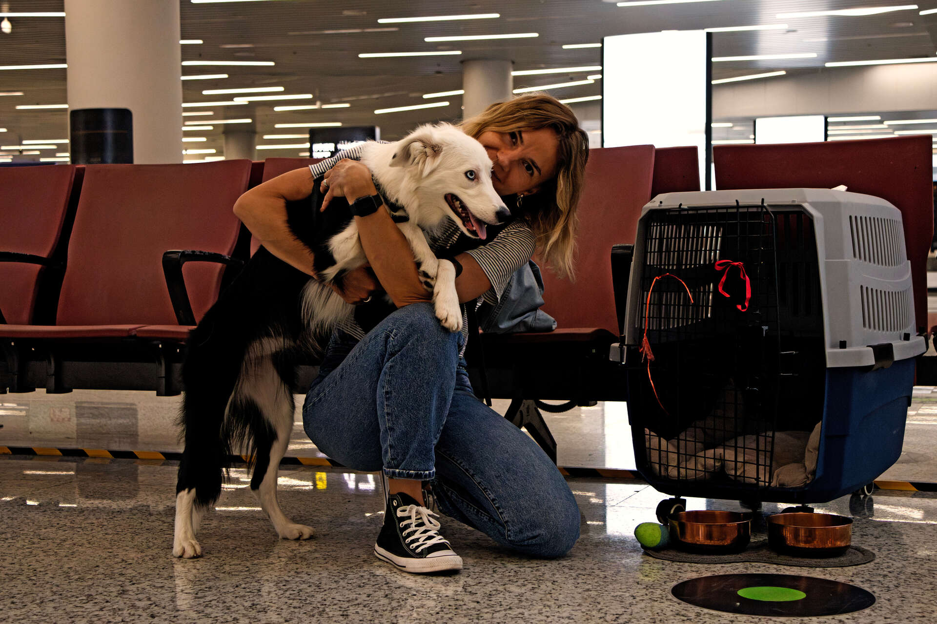A woman hugging a dog next to a travel carrier at an airport