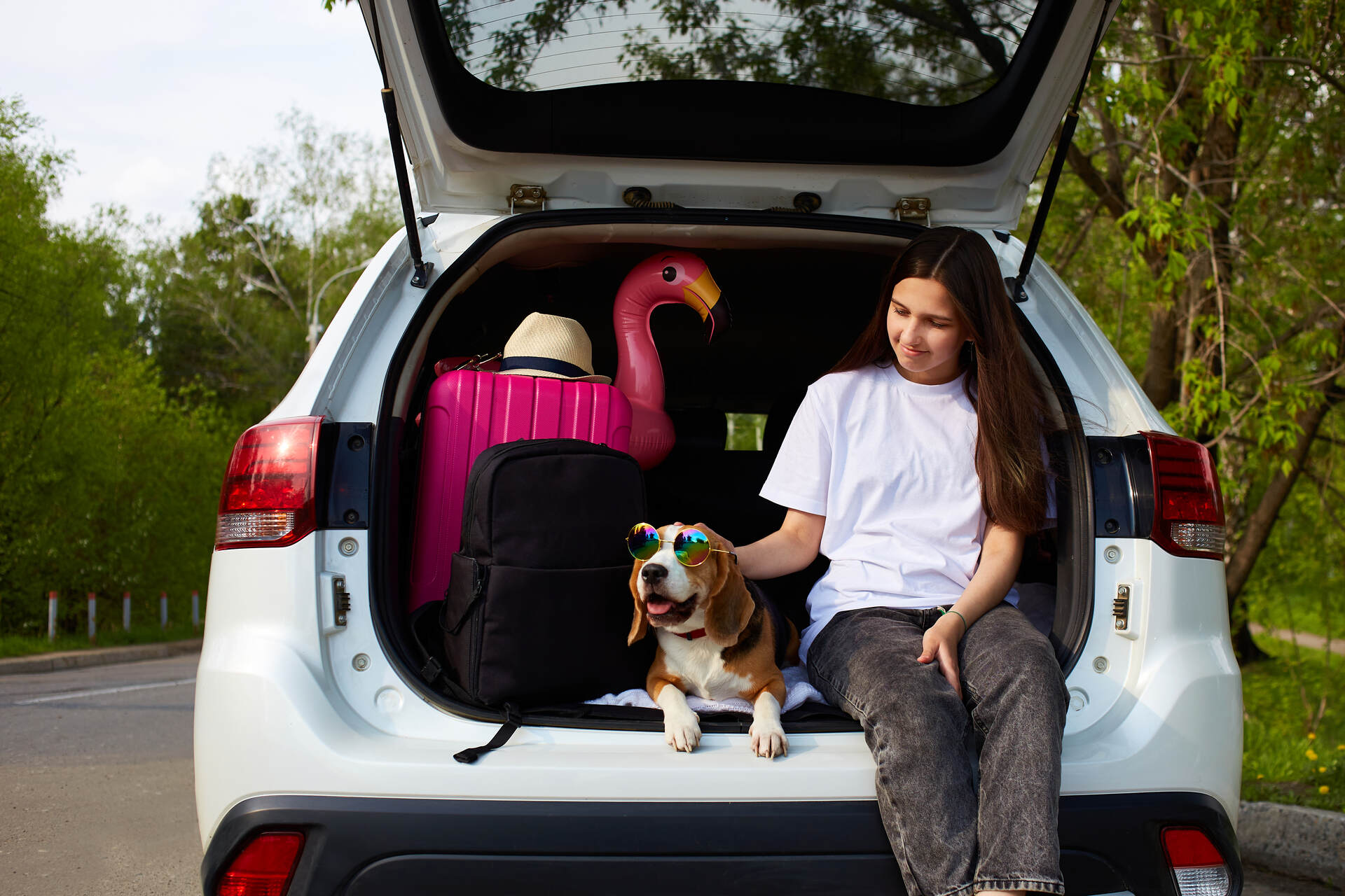 A girl sitting in the trunk of a car with a dog
