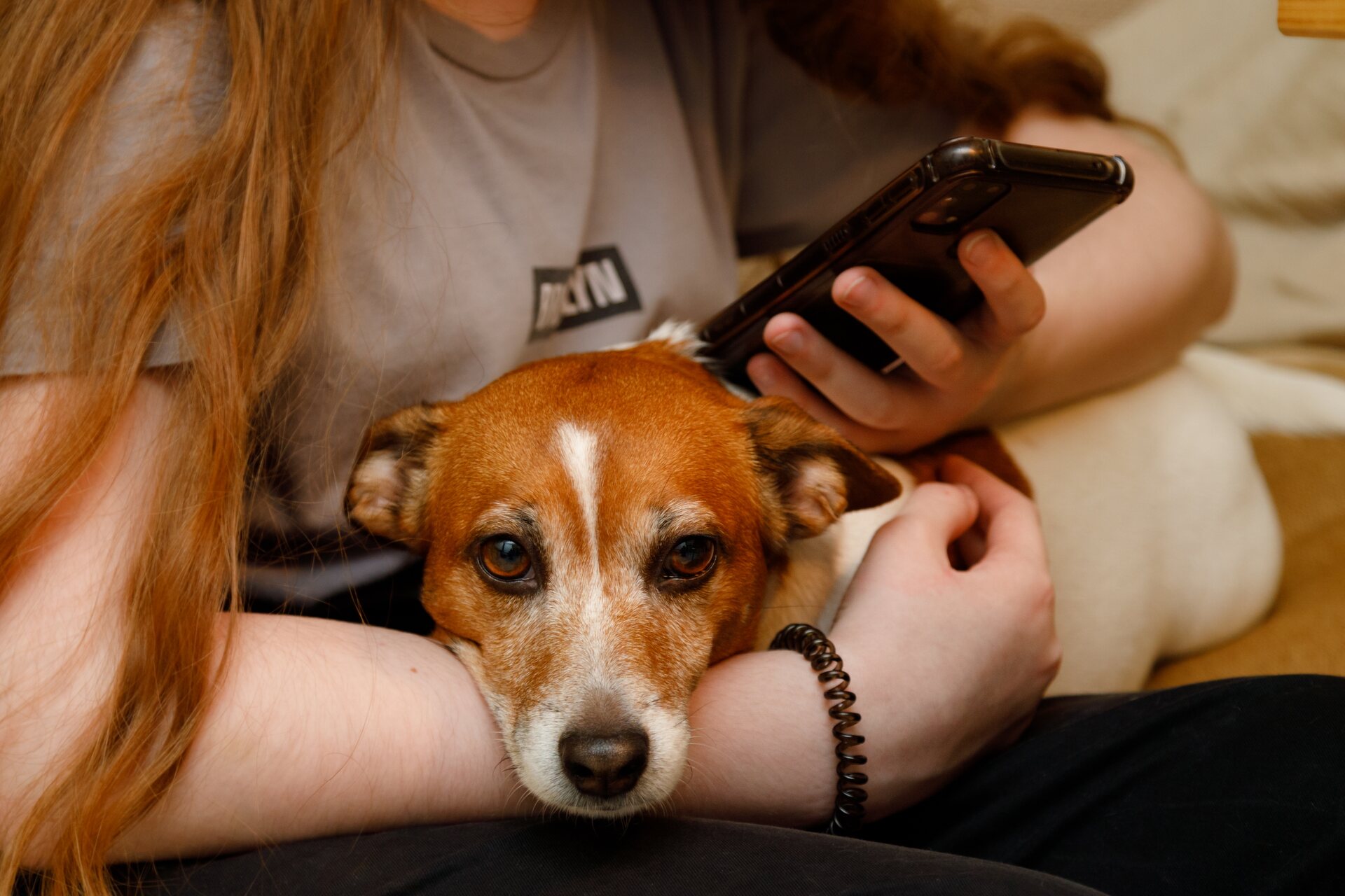 A woman cuddling her dog while checking her phone