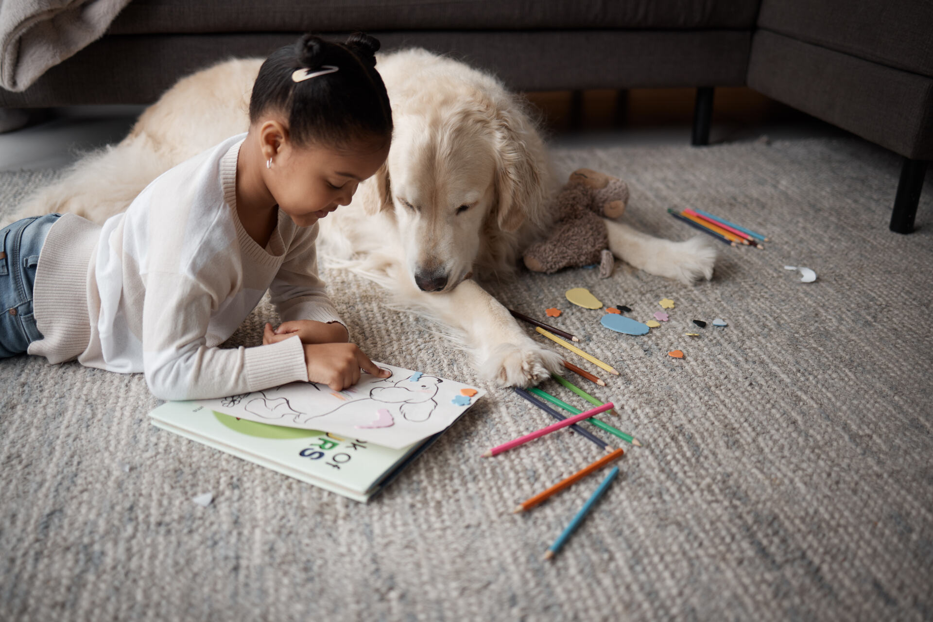 A little girl coloring a page in her box next to a dog
