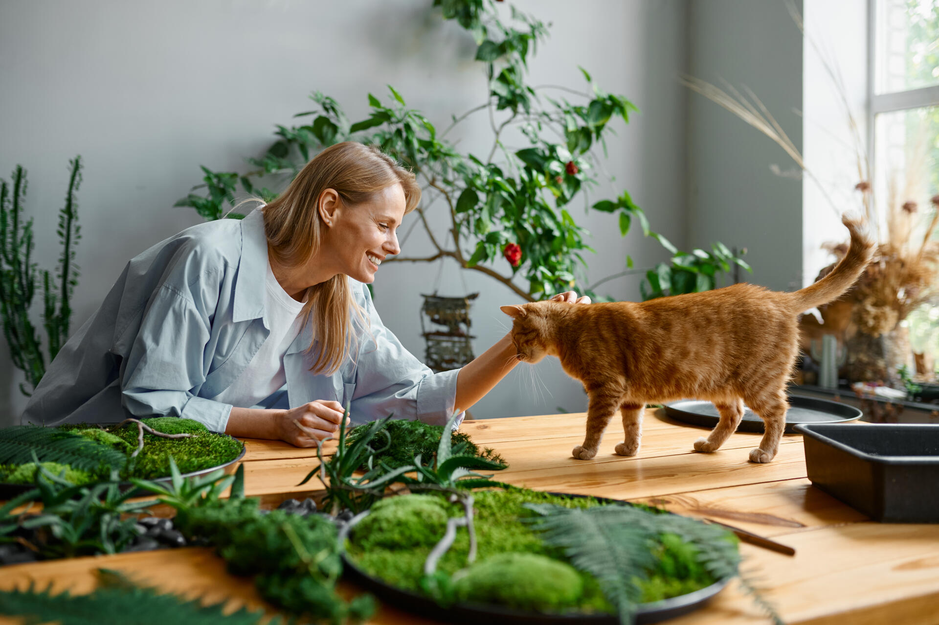 A woman petting a cat in a house filled with indoor plants