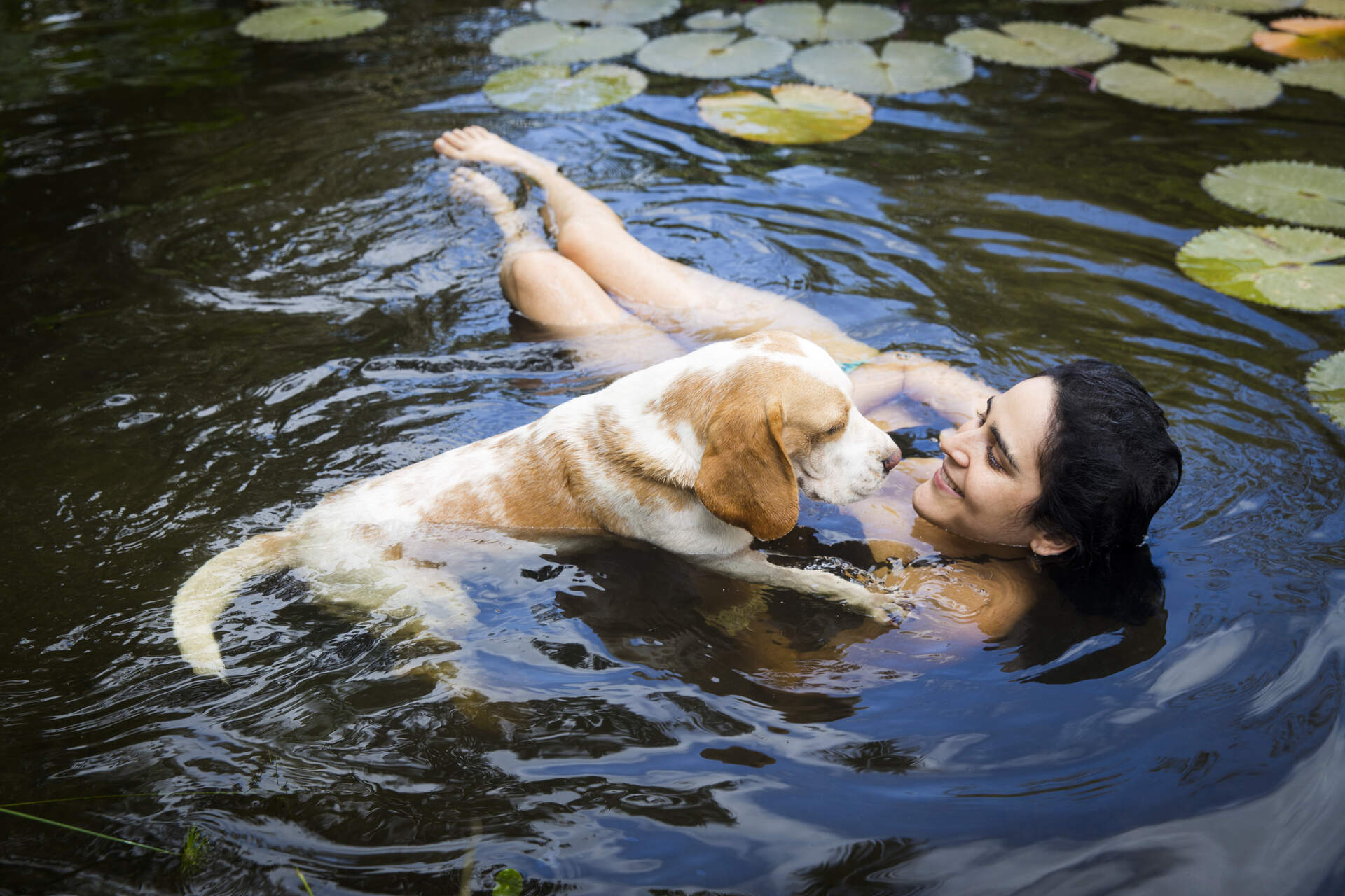 A woman swimming with her dog in a pond