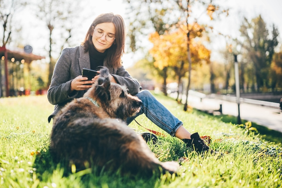 Frau sitzt mit ihrem Hund in der Wiese