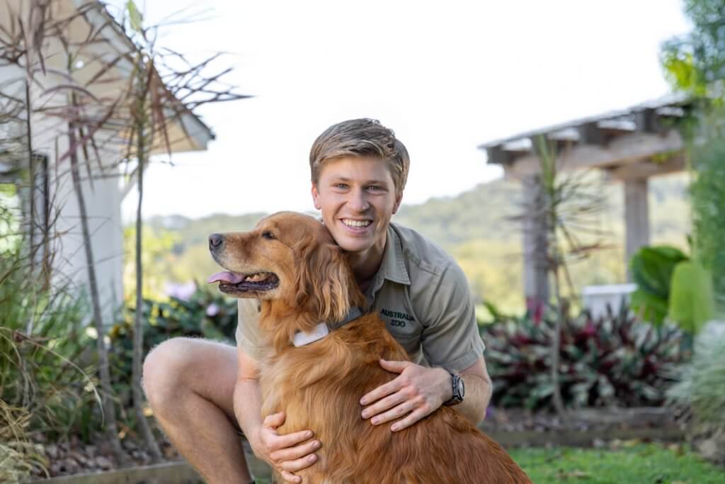 Robert Irwin cuddling a dog with a Tractive tracker in a garden