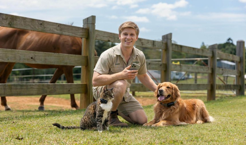Robert Irwin poses outdoors with a dog and cat wearing Tractive Smart Trackers