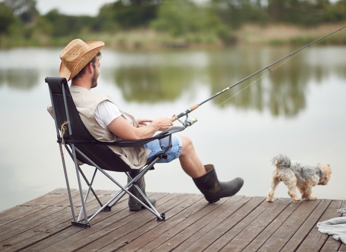 Mann angelt an einem Steg mit kleinem Hund