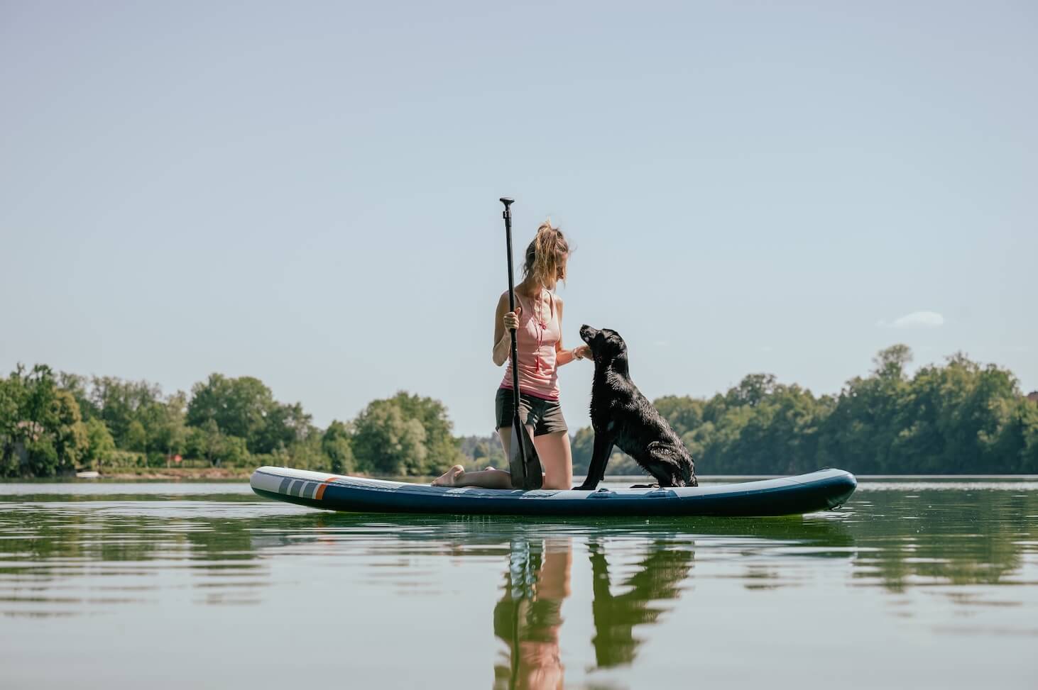 Frau mit ihrem Hund auf einem SUP-Board am Wasser